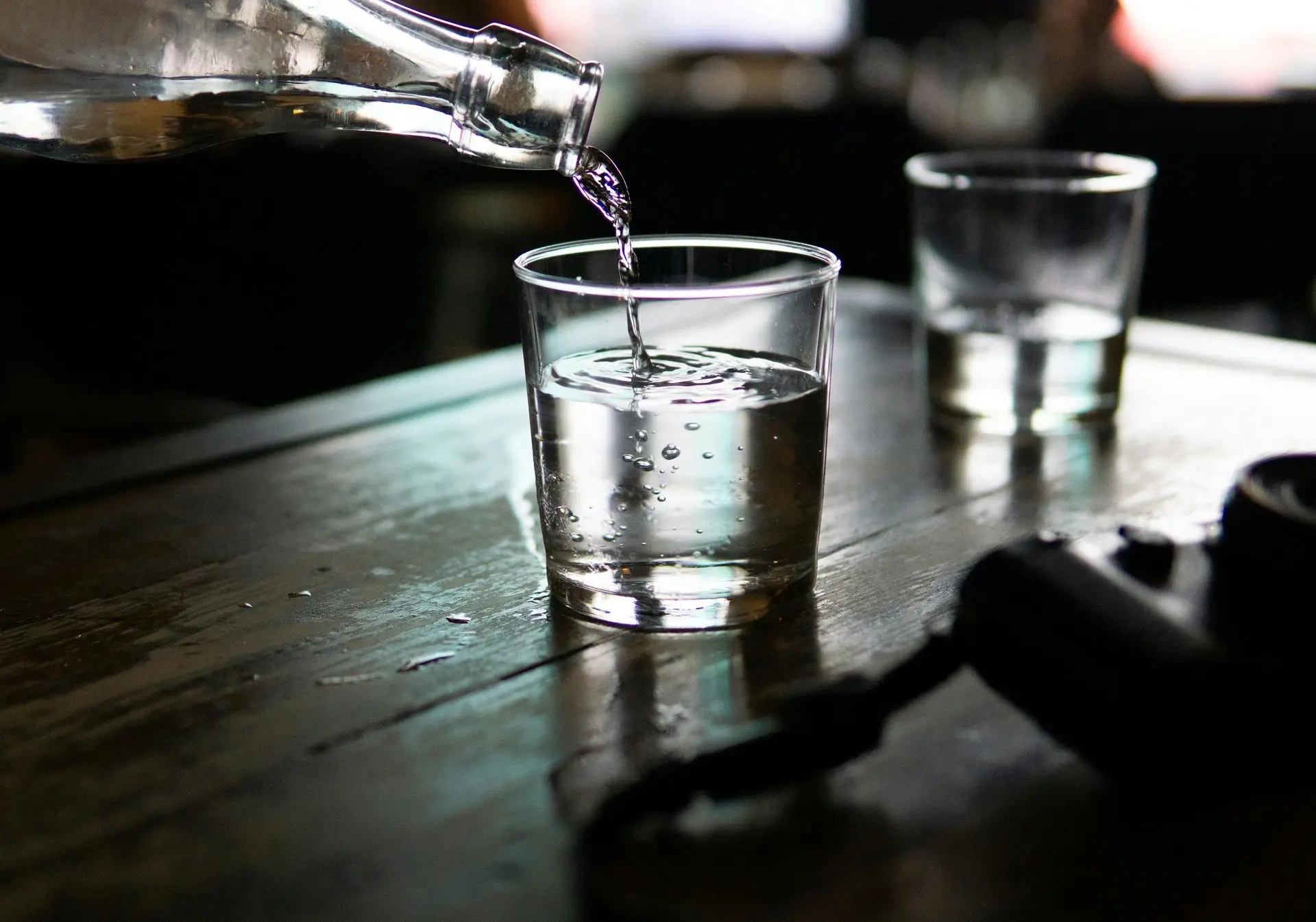Filtered water being poured into a glass from a bottle on a wooden table, symbolizing personalized care and quality hydration